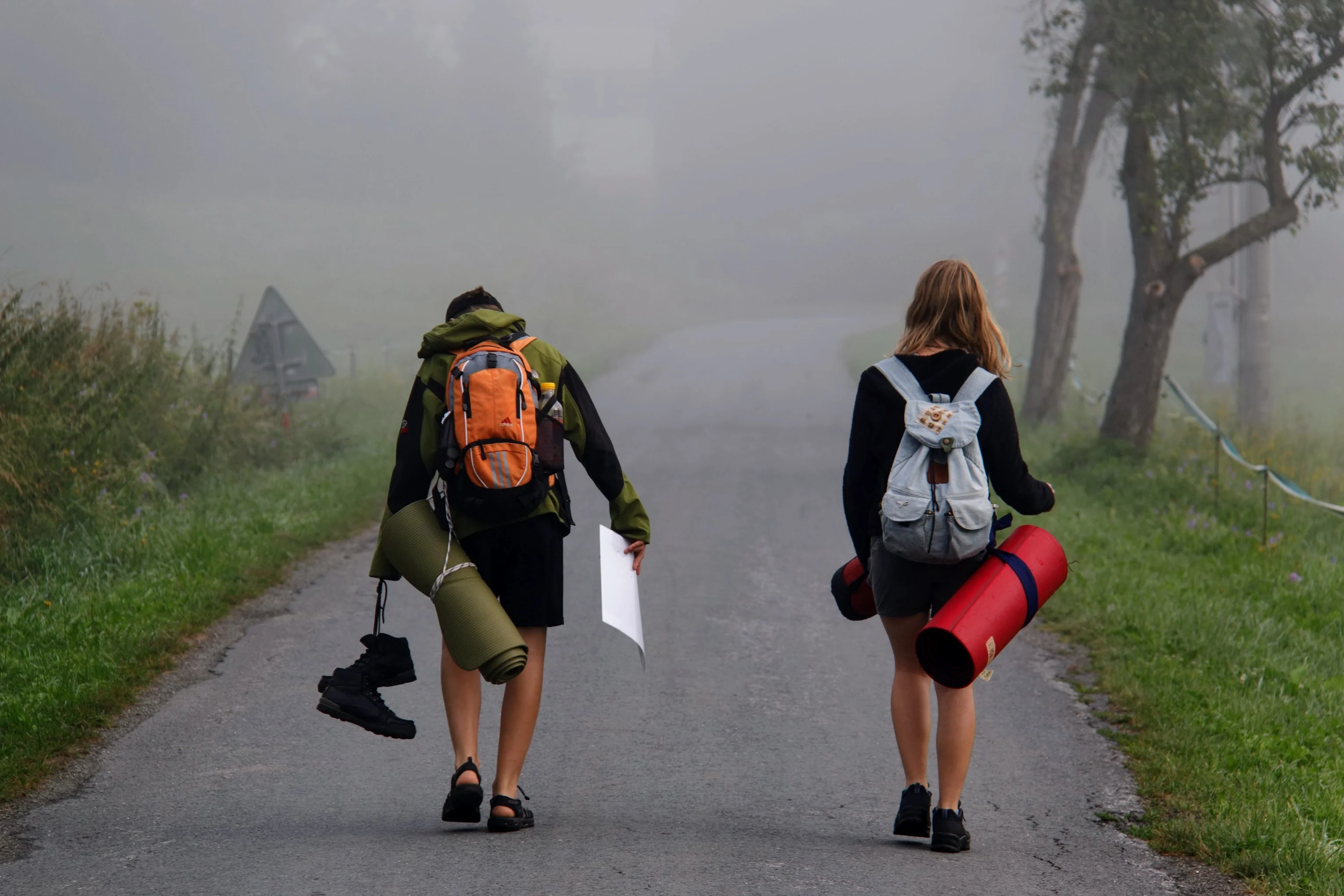 Two hikers carrying packs and camping mats along a misty trail
